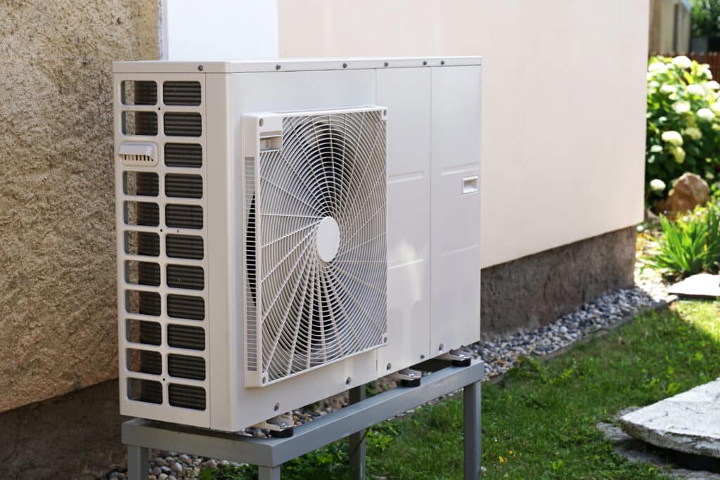 Heat pump on a lifted surface on side of home.